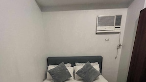 A neatly made bed with a dark headboard, two pillows, and a pair of rolled towels.