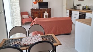 Une pièce de taille modeste comprenant un lit, une table à manger avec des chaises, un petit coin cuisine et une fenêtre avec des rideaux.