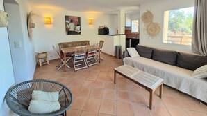 A modern living room with a sofa, a dining table with chairs, a wicker chair, and a small table.