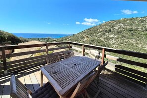 Um deck de madeira com mesa e cadeiras, com vista para a paisagem costeira.