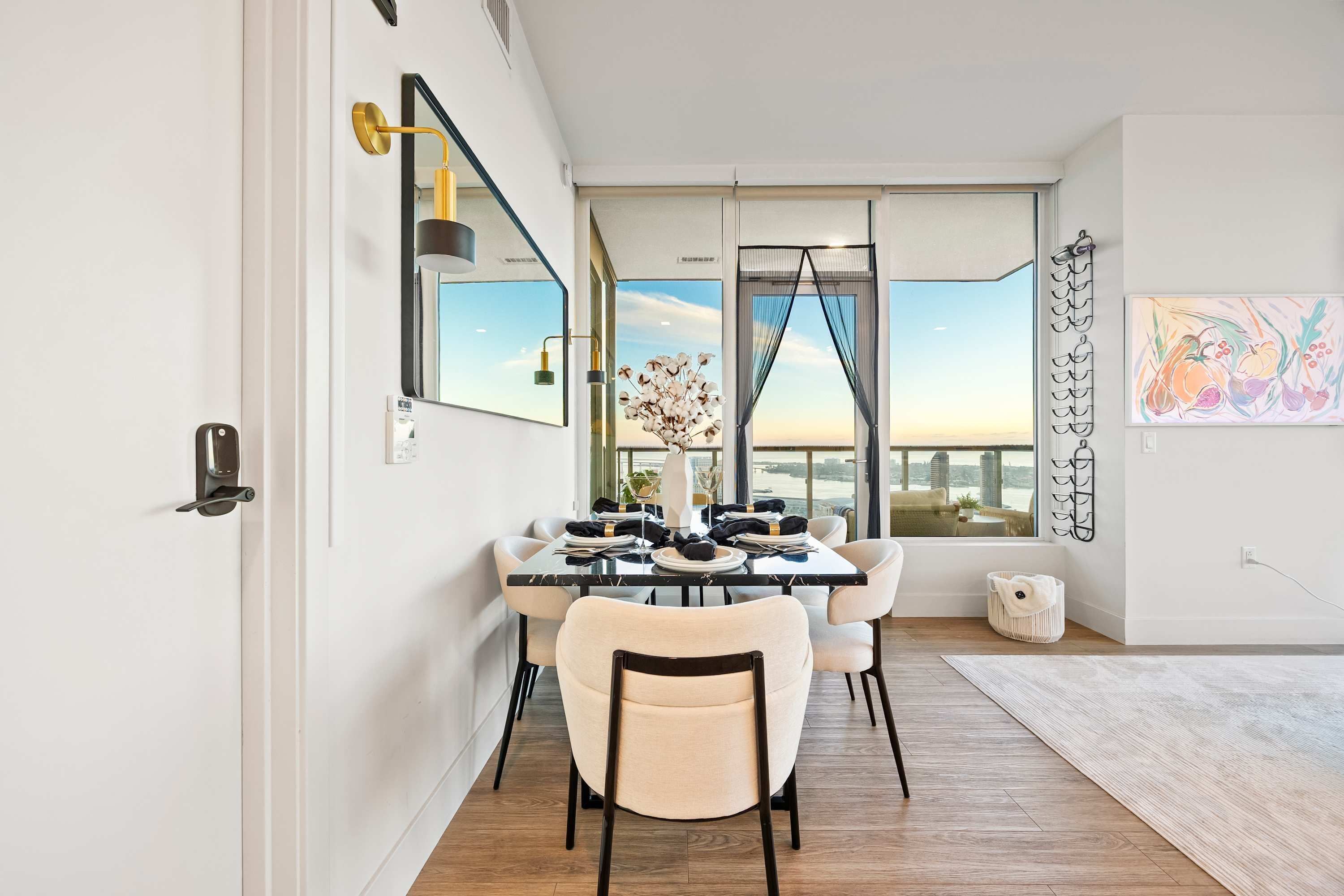 Un comedor moderno con un amplio ventanal, una mesa de comedor dispuesta con platos y vasos, y un florero con flores.