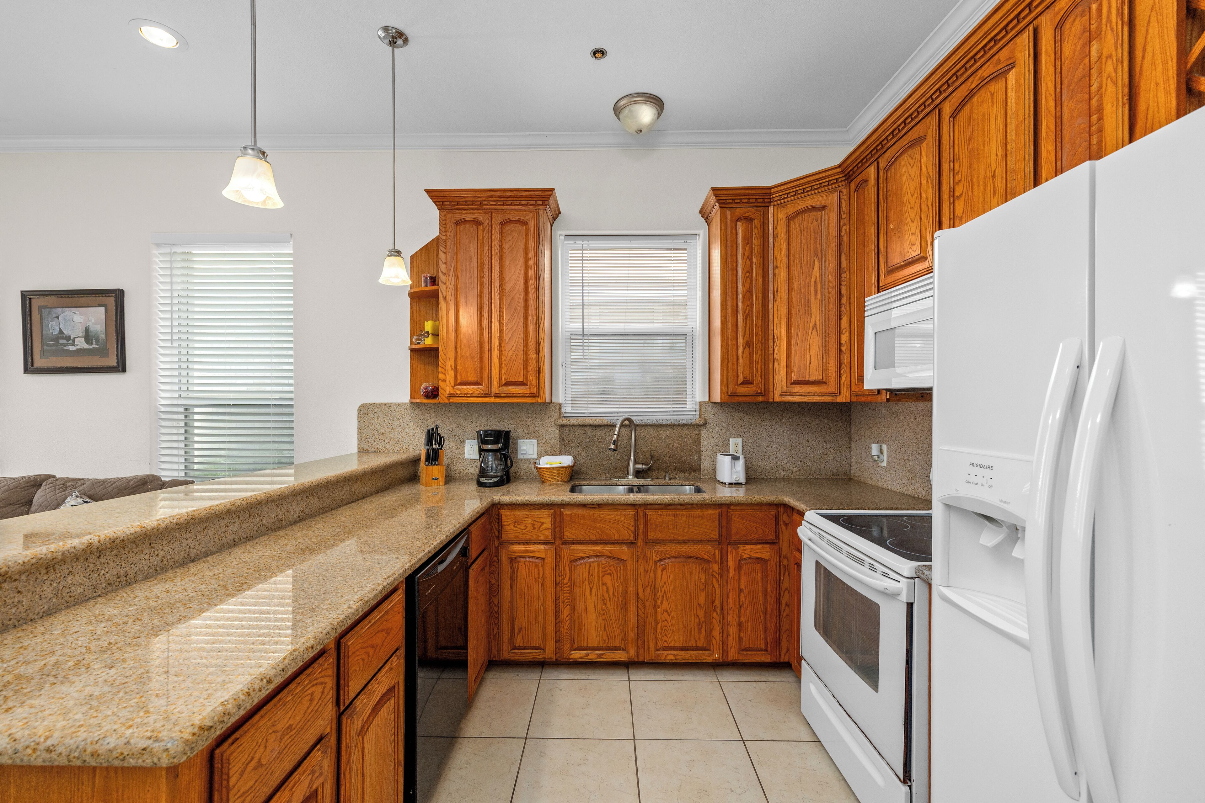 A kitchen with wooden cabinets, granite countertops, a white refrigerator, a microwave, and an oven.