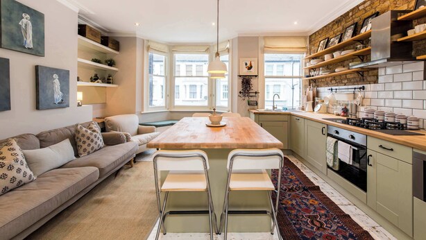 A modern kitchen with a central island, built-in shelves, and a dining area with a sofa and chairs. - Stunning 2-bedroom Flat in Fulham (London)