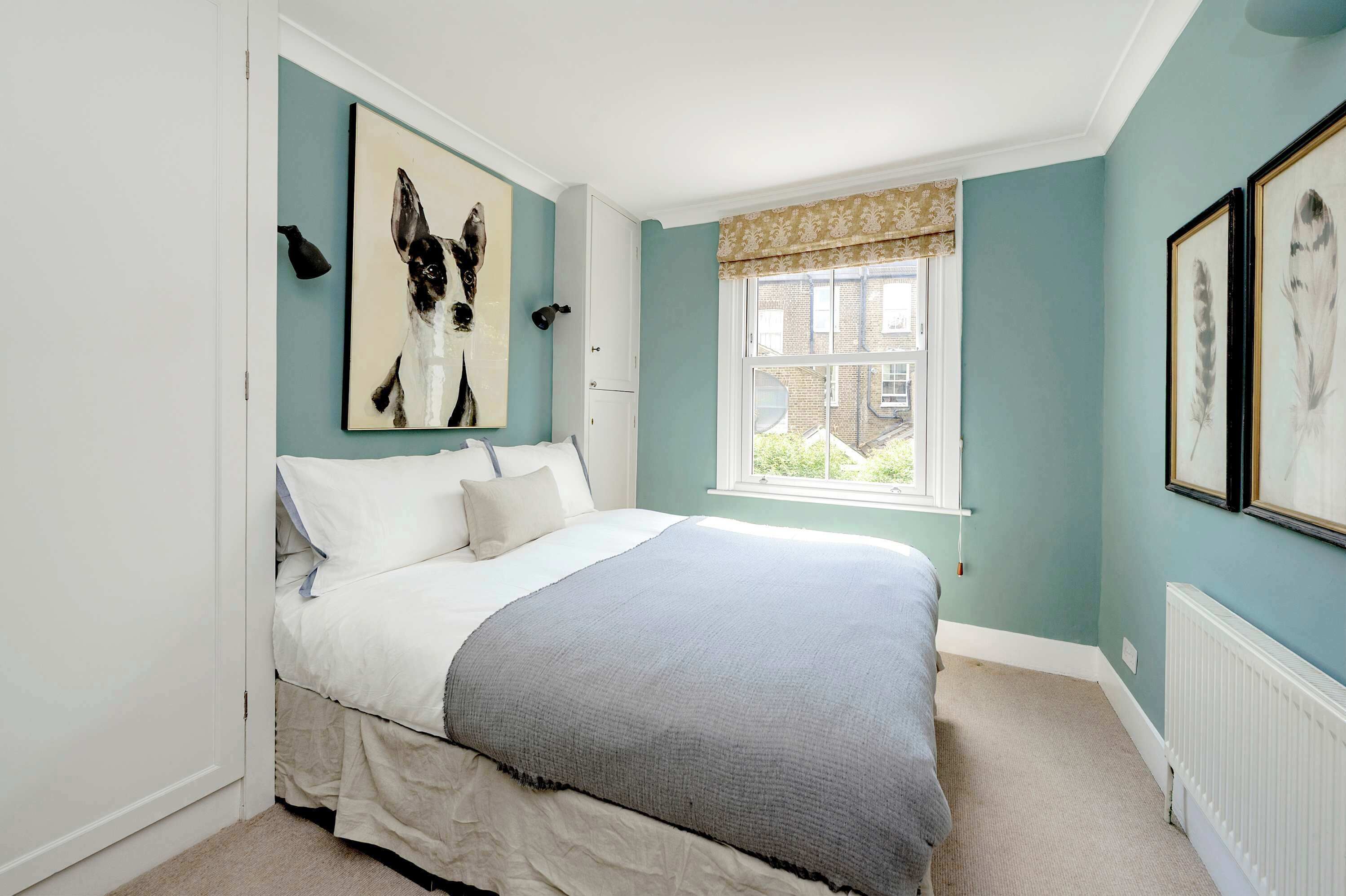 Un dormitorio con cama, ventana con cortinas y decoración en la pared.