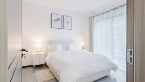 Ein modernes Schlafzimmer mit einem großen Bett, zwei Nachttischen mit Lampen, Blick auf die Stadt durch ein großes Fenster und zwei gerahmte Tierabbildungen an der Wand.