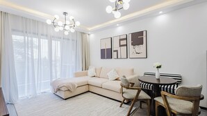 Ein modernes Wohnzimmer mit einem beigefarbenen Ecksofa, einem runden Esstisch mit Stühlen und einer Chandelüster.