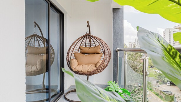 Ein Balkon mit zwei Hängestühlen aus Rattan, einer Topfpflanze und Blick auf die Stadt.