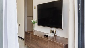 Ein modernes Wohnzimmer mit einem großen Flachbildfernseher an der Wand, einem Holztischchen mit Blumenvase und einer Tür zu einem anderen Raum.