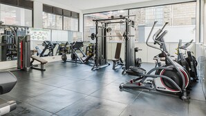 Ein modernes Fitnessstudio mit unterschiedlichen Trainingsgeräten, großen Fenstern und einem sauberen, gefliesten Boden.