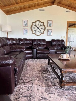Un salon avec un canapé d’angle en cuir marron foncé, un tapis à motifs et une table basse en bois.