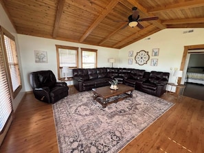 Un salon doté d’un plafond en bois, d’un grand canapé d’angle en cuir marron foncé, d’une table basse en bois et d’un tapis à motifs.