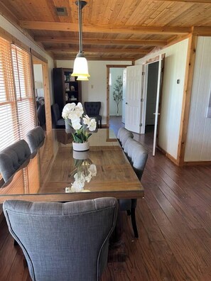 Un coin repas avec une table en bois, des chaises à revêtement gris et un vase rempli de fleurs blanches.