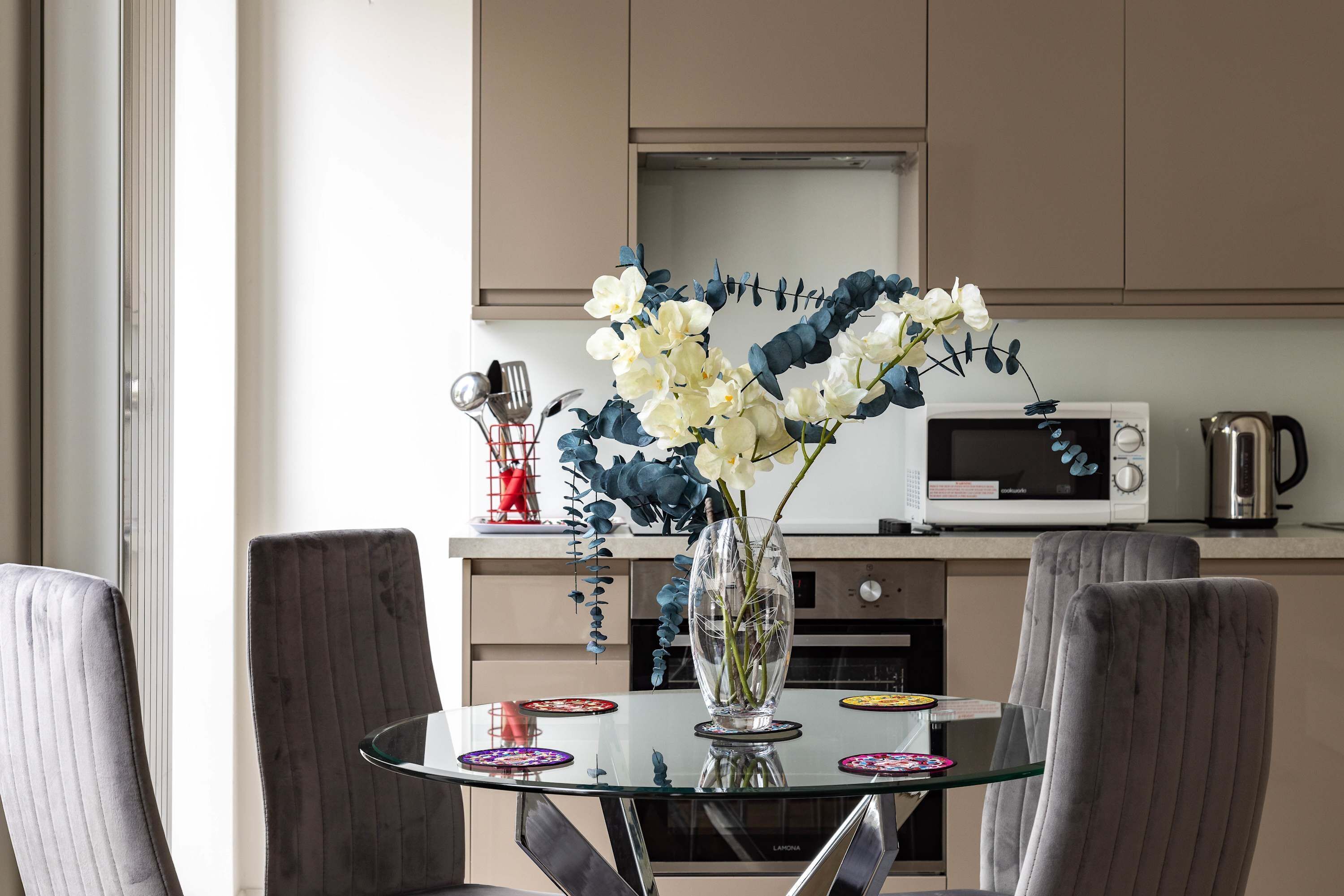 A modern kitchen with a microwave, kettle, and a vase with flowers on the counter.
