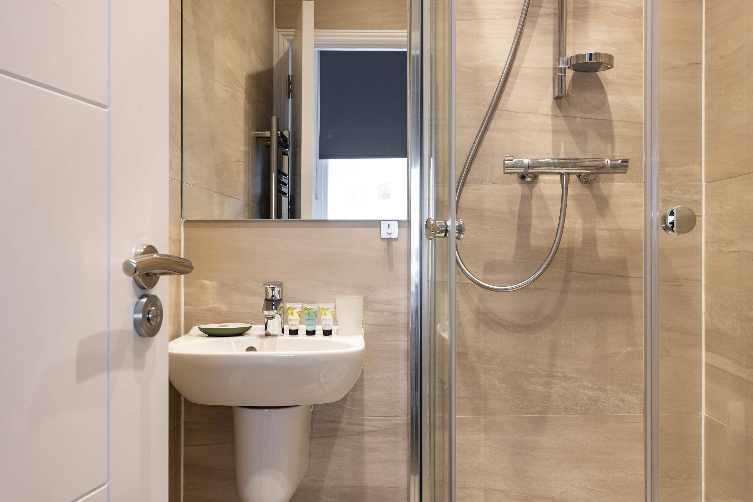 A modern bathroom with a glass shower enclosure, a sink with toiletries, and a mirror.