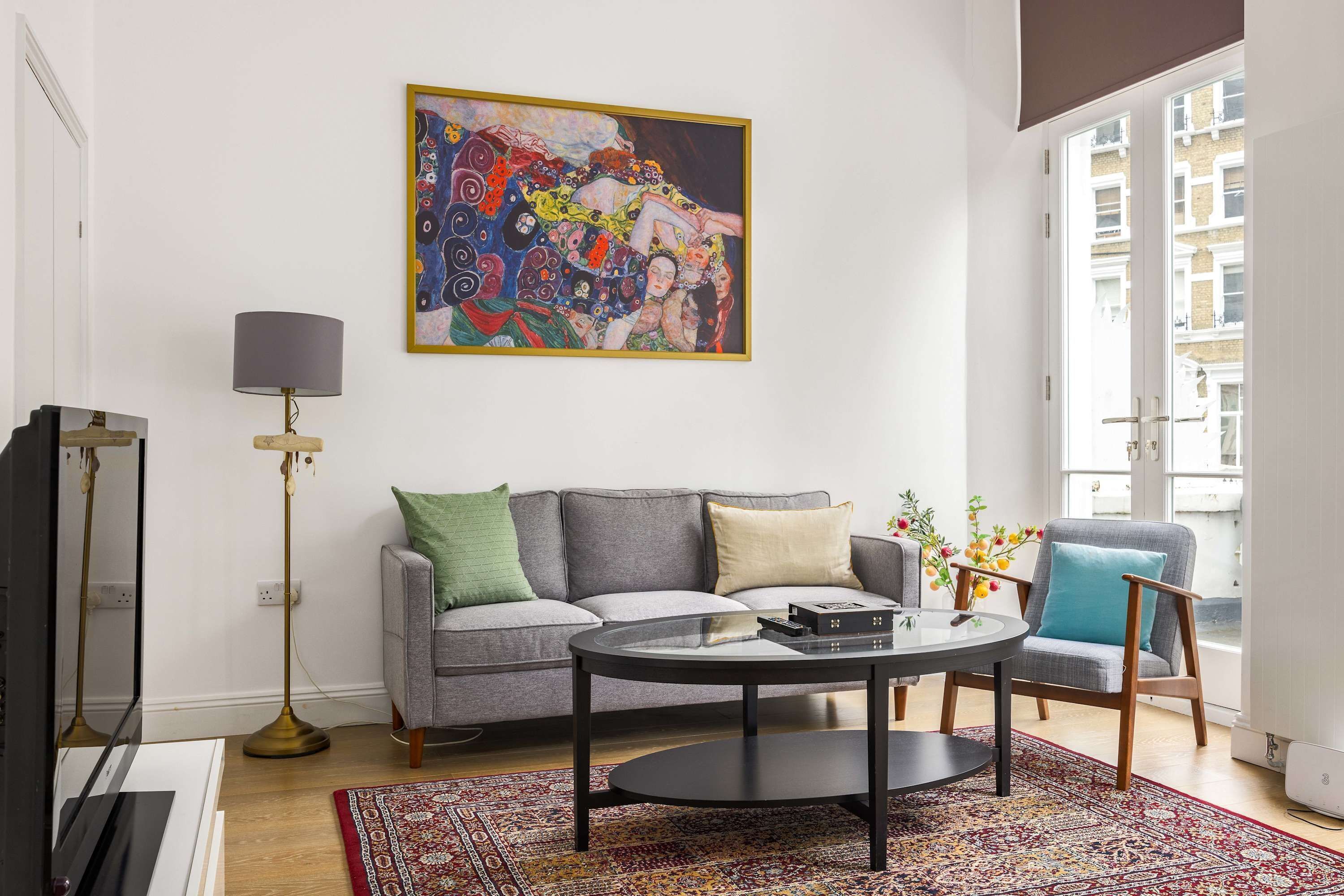 A living room with a grey sofa, a round coffee table, a floor lamp, and a colorful abstract painting on the wall.