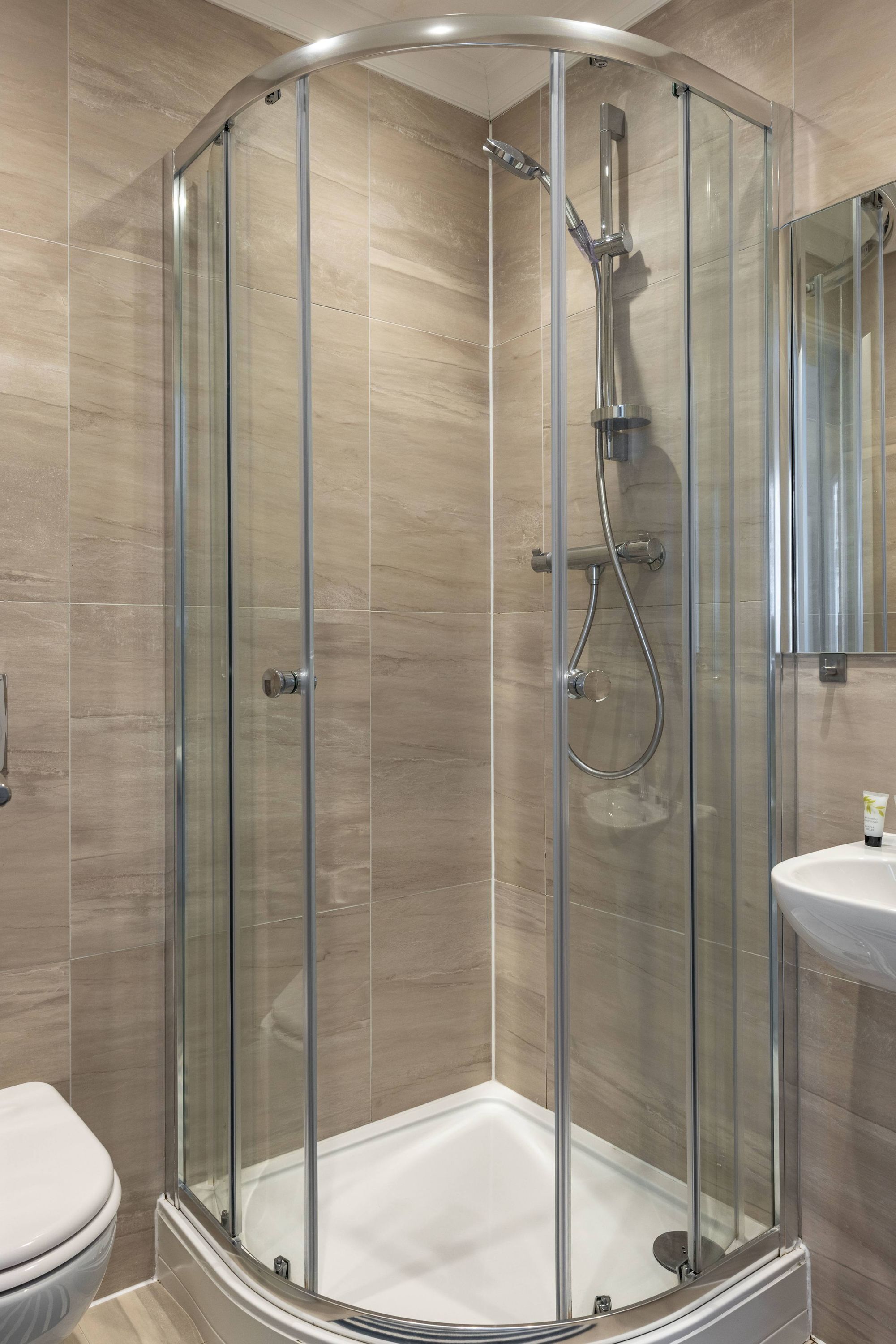 A modern bathroom with a glass-enclosed shower, a white toilet, and a sink with a mirror above it.