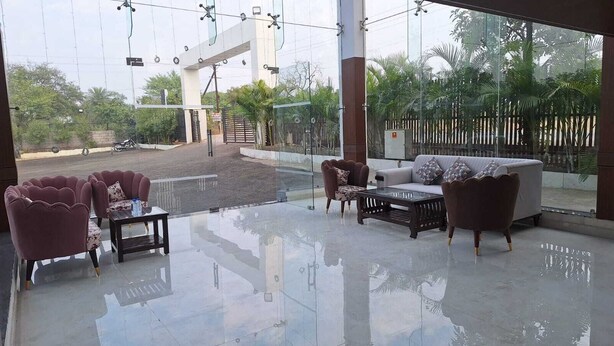 A spacious outdoor seating area with modern furniture, a glass floor, and a view of a gate and greenery. - Mango Retreat Hotel and Resort (Bhopal)