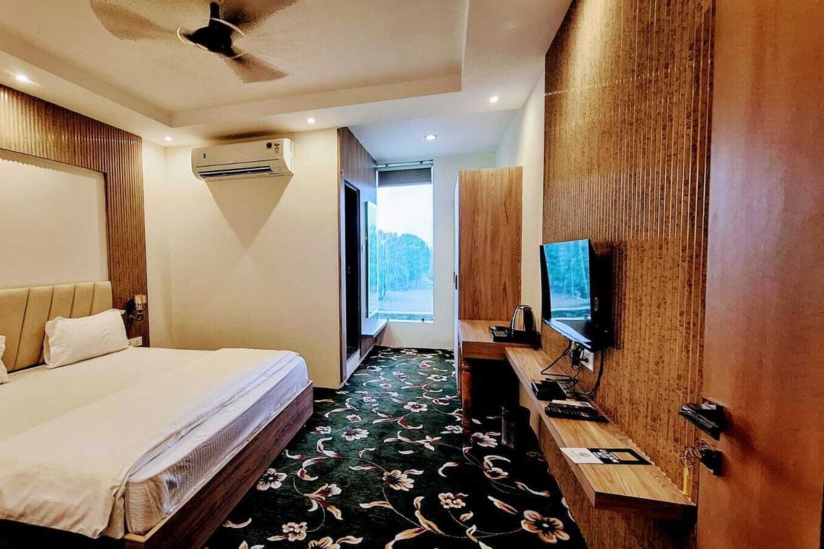 Una habitación de hotel con una cama, un escritorio con computadora, un televisor y un equipo de aire acondicionado.