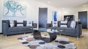 A modern living room with two grey sofas, a glass coffee table, and abstract wall art.