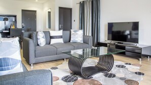 A modern living room with a grey sofa, a glass coffee table, a TV, and a patterned rug.