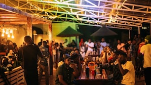 A crowded outdoor dining area with tables and chairs, a wooden structure, and string lights.