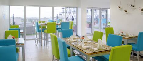 Un comedor con mesas y sillas, ventanas amplias y vista a la ciudad.