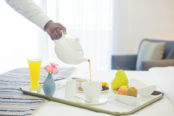 A breakfast tray with a teapot pouring tea, a glass of orange juice, a vase with flowers, and a plate with fruits and a pastry. - Amaryllis Hotel (Blantyre)