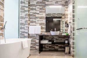 A modern bathroom with a stone mosaic wall, a white bathtub, a black vanity with a sink, and a glass shower enclosure. - Amaryllis Hotel (Blantyre)