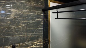 A bathroom with a marble wall, a showerhead, and a glass shower enclosure. - NSC 1085 (Rio de Janeiro)