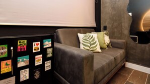 A modern living room with a grey sofa, a black entertainment unit with various stickers, and a unique curved wall design. - NSC 1085 (Rio de Janeiro)