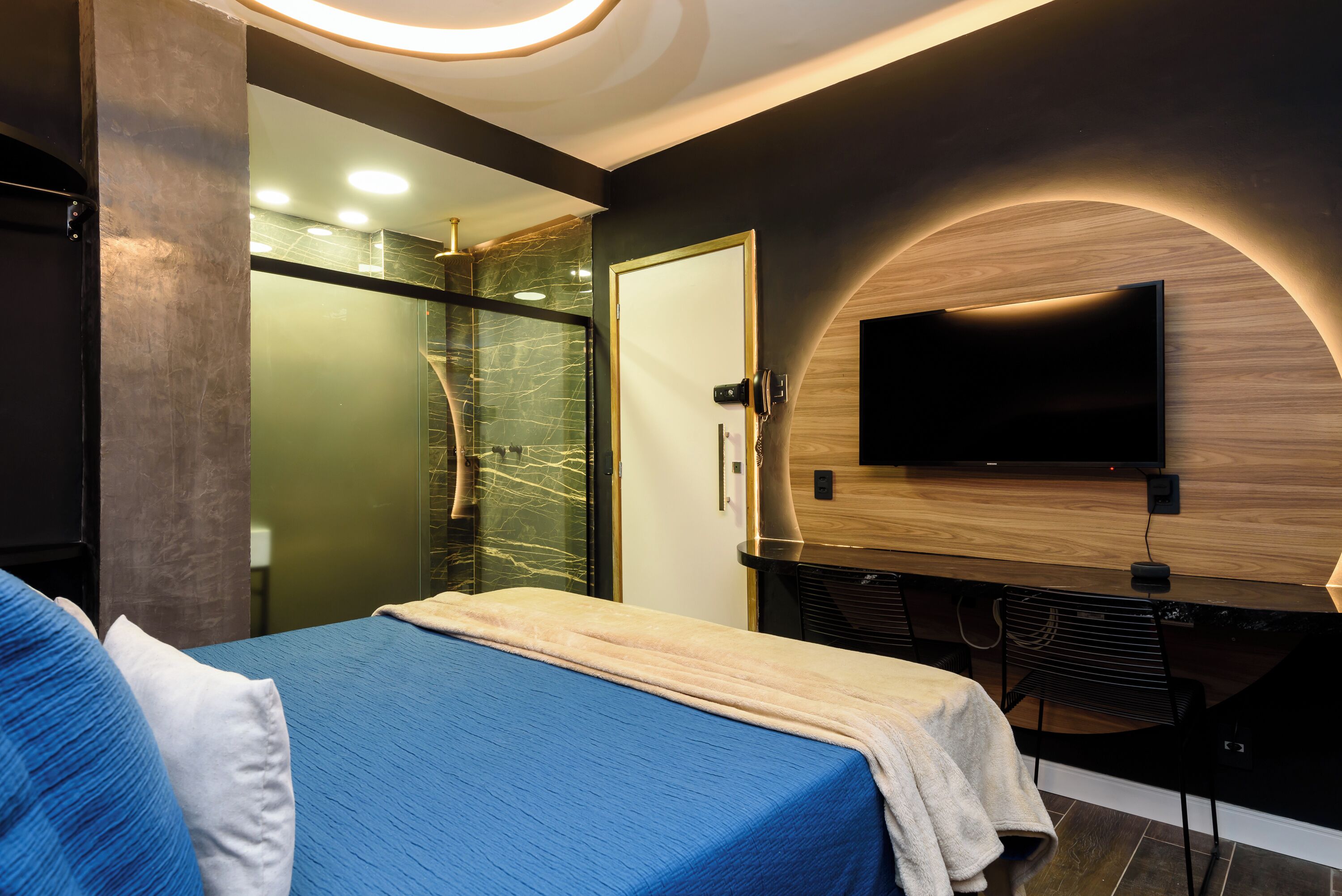 Een moderne hotelkamer met een bed, een aan de muur bevestigde televisie en een douchecabine van glas.