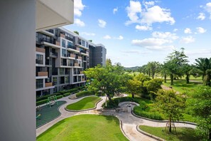 Un moderno edificio de apartamentos con varios balcones y un patio bien cuidado, con vegetación y un parque infantil.