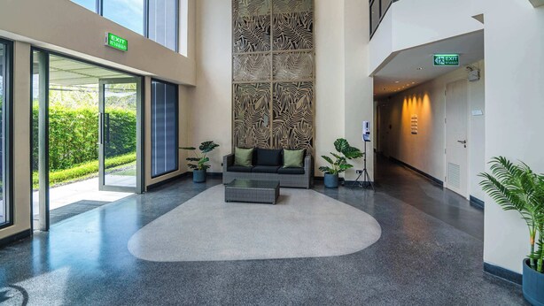 Un hall d’entrée agrémenté d’un grand panneau décoratif, d’un canapé avec des coussins, de plantes en pot et d’un panneau indicateur de sortie.