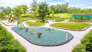 A playground with various play equipment, surrounded by well-maintained grass and trees. - Skypark Aurora, One Bedroom 2312 1B Deluxe (Choeng Thale)