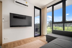 Una sala de estar moderna con un televisor de pantalla plana, un sofá y grandes ventanales con vistas a la vegetación.