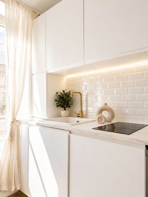 A modern kitchen with white cabinetry, a gold faucet, and a potted plant.