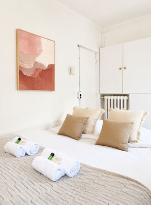 A hotel room with a bed, pillows, a radiator, a painting, and towels.