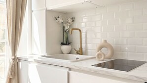 Eine moderne Küche mit weißen Schränken, einer weißen Fliesenspiegel und einem goldenen Wasserhahn, dazu ein Orchideenstrauß im Topf.