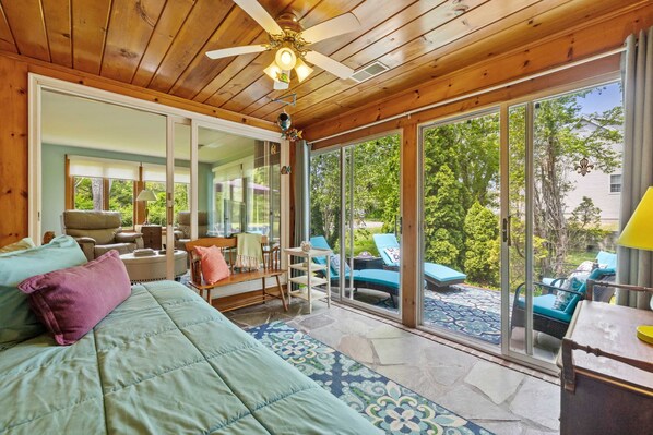 A bedroom with a bed, a ceiling fan, a large sliding glass door leading to a patio with outdoor furniture.