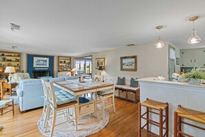 A spacious living room with a wooden dining table, a sofa, and a kitchen area with a white countertop.