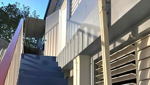 A set of exterior stairs leading to a building with white siding and a window with horizontal blinds.