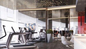 Un gimnasio moderno con cintas de correr, bicicletas estáticas y una recepción con una pared de acento rojo.