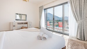 Ein Hotelzimmer mit einem großen Bett, einem Schminktisch mit Spiegel und Blick auf Berge durch eine Schiebeglastür.