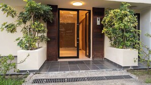 Entrada de hotel con puerta de cristal, plantas en macetas y suelo de baldosas.