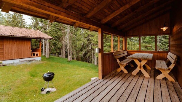 A wooden deck with a table and benches, a barbecue grill, and a view of a forested area. - Lima Alpine Lodges - Almhaus Theresia (Sauerwald)