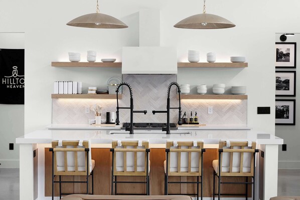 Une cuisine moderne dotée d’un îlot central, de tabourets de bar, de luminaires suspendus et d’un revêtement mural disposé en motif chevrons.