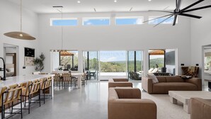 A spacious living area with a large window, a ceiling fan, and a bar area with chairs. - Labor Day Getaway | Heated Pool + Spa + Epic Views (Canyon Lake)