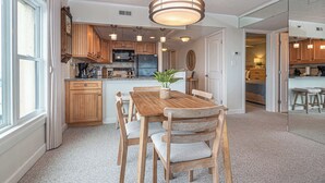 A kitchen with wooden cabinets, a dining table with chairs, a hanging light fixture, and a plant on the table. - Ocean Front Condo with Pool (Ocean City)