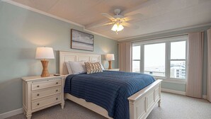 A bedroom with a bed, nightstands, a ceiling fan, and a large window. - Ocean Front Condo with Pool (Ocean City)