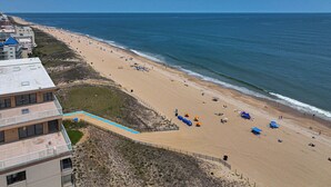 A beach with a long stretch of sand, a few umbrellas, and a building with a flat roof on the left. - Ocean Front Condo with Pool (Ocean City)